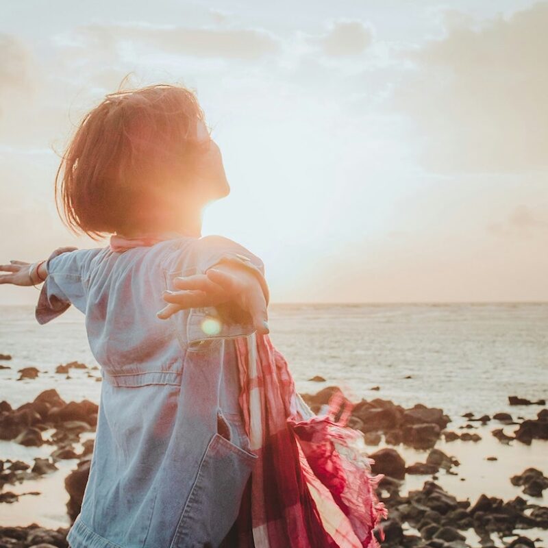 Woman standing on beach with sun on face and arms outstretched