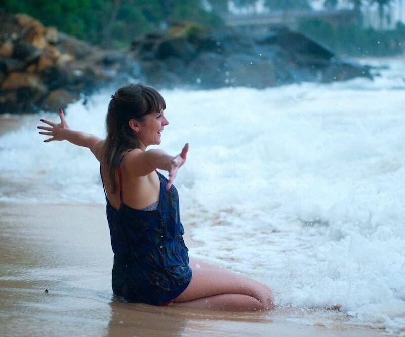 woman sitting on shoreline with arms outstretched, smiling