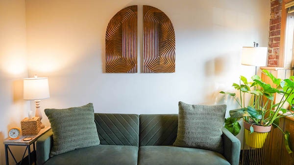 Green sofa under wooden wall art in bright room