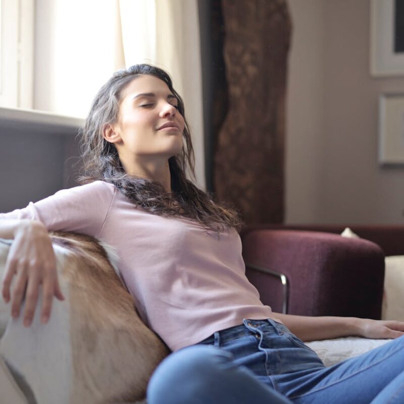 photo-of-woman-in-pink-long-sleeve-shirt-and-blue-denim-jeans-sitting-on-brown-sofa-with-her-eyes-closed