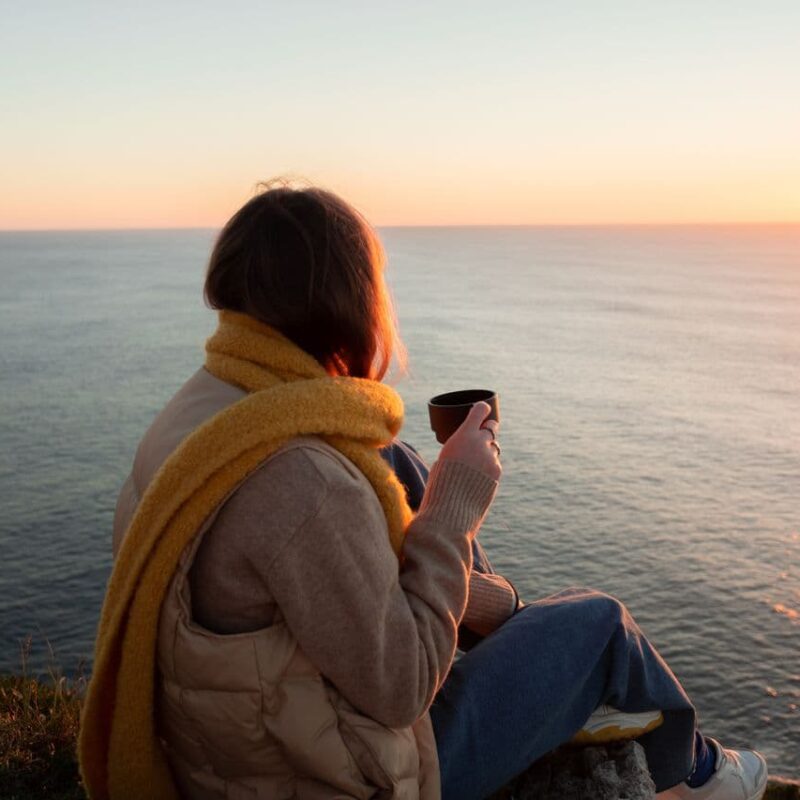 a-woman-sitting-near-the-cliff-holding-a-mug