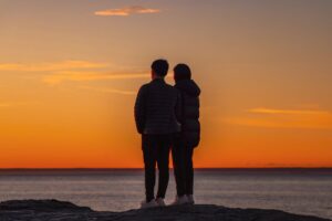 photo-of-couple-standing-on-a-rock-near-ocean