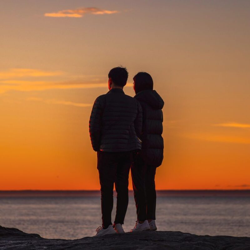 photo-of-couple-standing-on-a-rock-near-ocean