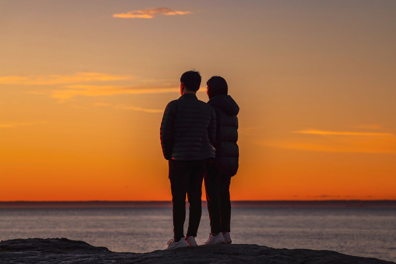 photo-of-couple-standing-on-a-rock-near-ocean